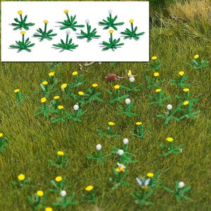 May include: A collection of miniature artificial dandelion plants featuring green serrated leaves and stems with either bright yellow flower heads or white spherical seed heads, displayed both as a group and scattered across a grassy surface.