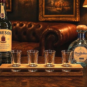 May include: A bar scene featuring a bottle of Jameson Irish Whiskey and a bottle of Don Julio tequila. Four shot glasses sit on a wooden tray. The scene is set on a dark wooden table with a leather couch in the background.