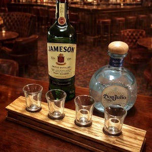 May include: A bar scene featuring a bottle of Jameson Irish Whiskey and a bottle of Don Julio Blanco Tequila. Four shot glasses sit on a wooden serving tray. The background shows a dimly lit bar with seating.