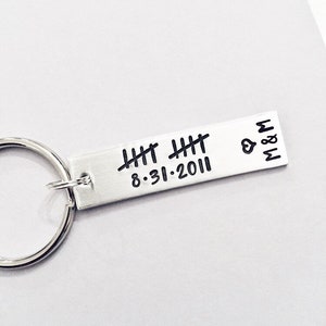 May include: Silver keychain with a silver bar engraved with the date 8.31.2011 and tally marks. The bar also has a heart and the letters M & M.