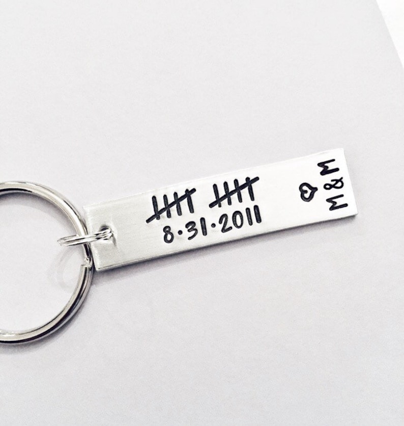 May include: Silver keychain with a silver bar engraved with the date 8.31.2011 and tally marks. The bar also has a heart and the letters M & M.