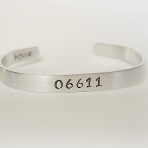 May include: Silver cuff bracelet with the words "home" and "06611" engraved on it.