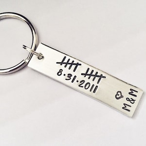 May include: Silver keychain with a rectangular tag engraved with the date 8.31.2011 and the initials M&M. The tag also has a series of hash marks.