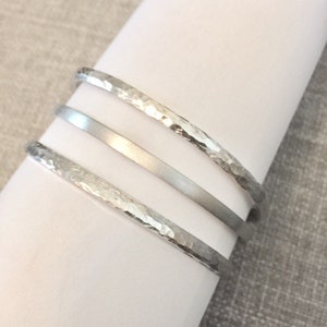 May include: Three silver bracelets, one smooth and two with a hammered texture.