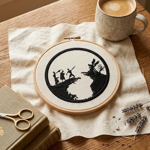 May include: A circular wooden embroidery hoop containing a piece of off-white fabric with a black thread silhouette design. The embroidery depicts three figures standing on a cliff edge facing a winged figure on an opposing cliff across a gap.