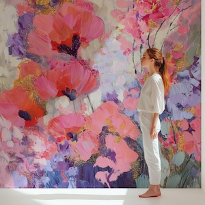 May include: Large floral painting with a palette of pink, purple, and gold. The artwork features bold brushstrokes and a textured appearance, showcasing a variety of flower types. The painting has a vibrant and expressive style, with a woman standing in front of it.