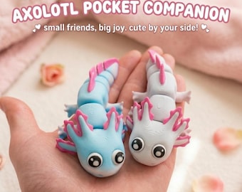 Può includere: Due piccole statuette articolate di axolotl, una azzurra e una bianca, entrambe con branchie rosa brillante e grandi occhi neri con riflessi bianchi. Il testo AXOLOTL POCKET COMPANION small friends, big joy. cute by your side! è visibile.
