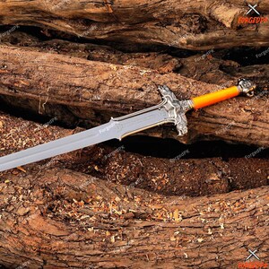 May include: A silver-colored sword with an orange handle and ornate silver crossguard. The blade is long and pointed, and the handle has a detailed design. The sword rests on a bed of rough-hewn wood.