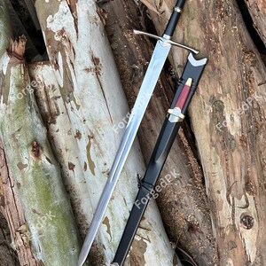 May include: A silver sword with a black handle and scabbard. The sword is lying on a pile of wooden logs.