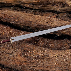 May include: A silver sword with a brown and gold handle resting on a pile of brown tree branches.