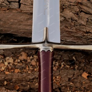 May include: Close-up of the crossguard of a medieval sword with a brown leather grip. The sword is made of polished steel and has a sharp point.