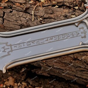 May include: A close-up of a silver-colored sword blade with etched symbols and a decorative handle. The blade has a polished finish and is set against a textured wooden background. The sword's design suggests a fantasy or historical theme.