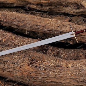 May include: A silver sword with a brown and gold handle lies on a bed of brown tree branches.