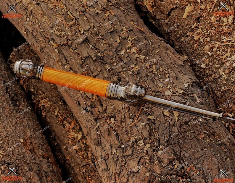 May include: A decorative dagger with a silver handle and a bright orange wrapped grip. The blade is silver and the dagger rests on a bed of brown wood.