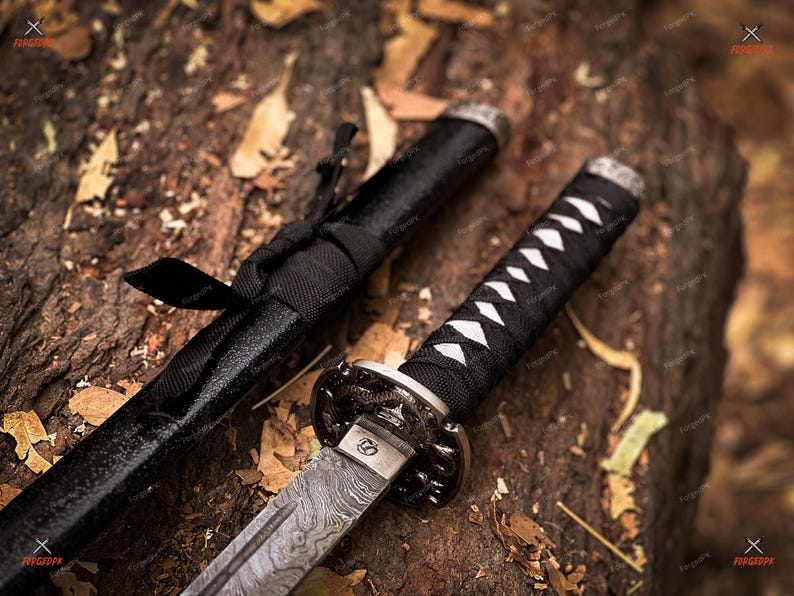 May include: Close-up of a katana sword with a black handle and scabbard. The blade has a unique pattern, and the handle is wrapped with white and black material. The sword rests on a textured, brown surface.