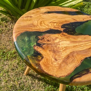 May include: A round wooden table top with a green and black epoxy resin inlay. The table has three wooden legs.