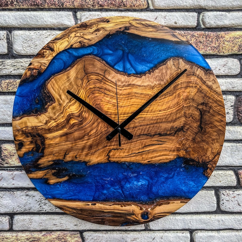 Puede incluir: Reloj de pared redondo de madera con un dise&ntilde;o &uacute;nico. La esfera del reloj presenta vetas de madera natural con un r&iacute;o de resina azul vibrante. Las manecillas negras indican la hora. Una pieza decorativa para cualquier habitaci&oacute;n.