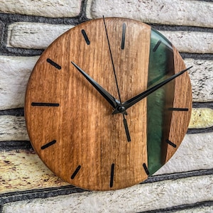 Könnte beinhalten: Eine runde Holzuhr mit schwarzen Zeigern und einer grünen Epoxidharzeinlage. Das Zifferblatt der Uhr hat schwarze römische Ziffern.