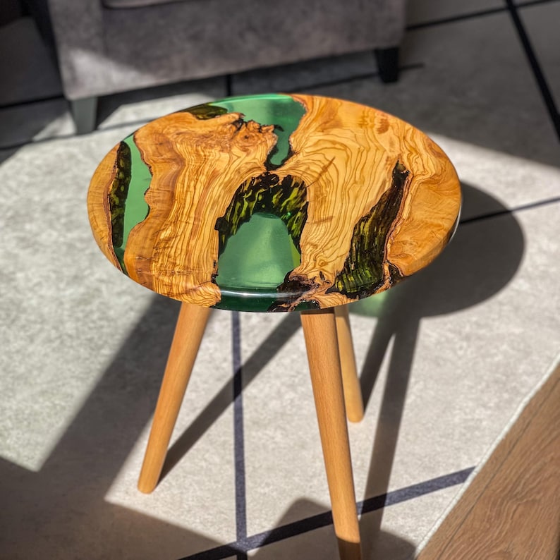 May include: A small wooden side table with three legs. The tabletop is made of olive wood and has a green epoxy resin inlay. The resin has a swirling pattern.