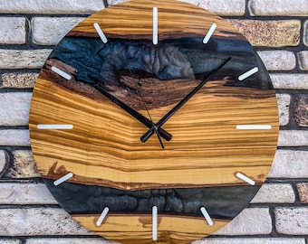 May include: A round wooden wall clock with a natural wood grain pattern and a dark blue resin river design. The clock features white hour markers and black hands. The clock is mounted on a brick wall.