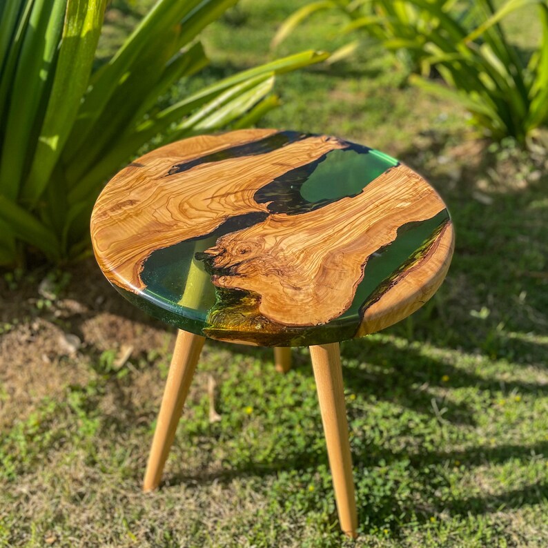 May include: Round wooden table with a green and black epoxy resin top. The table has three wooden legs.