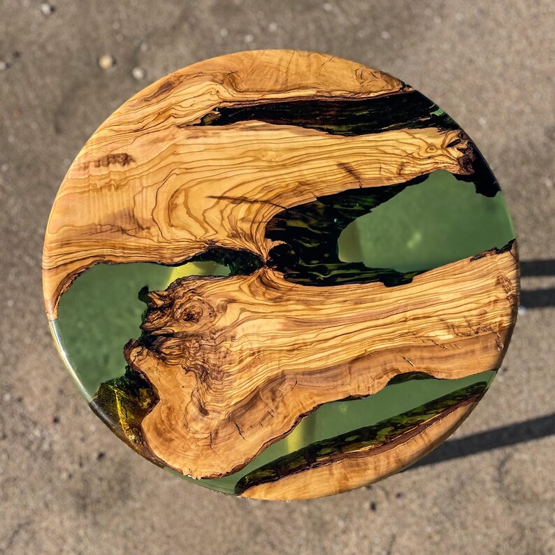 May include: Round wooden table top with a green epoxy resin inlay. The wood has a natural grain pattern and the resin has a smooth, glassy finish.