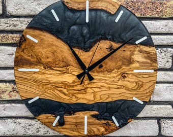 May include: A round wooden clock with a natural wood grain pattern and black resin accents. The clock features white hour markers and black hands. The clock is mounted on a brick wall.