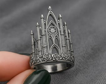 May include: A silver ring with a detailed design of a gothic cathedral. The ring is adorned with small rose-like details around the base.