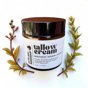 Puede incluir: Un tarro de crema de sebo con tapa marrón oscuro y etiqueta blanca. La etiqueta dice "tallow cream" y "MOISTURIZE I NOURISH I SOOTHE". El tarro contiene 118 ml. El tarro está rodeado de ramitas verdes.