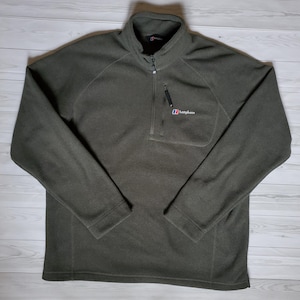 May include: Olive green fleece pullover with a quarter-zip closure and a small chest pocket. The Berghaus logo is visible on the pocket. The long-sleeved top has a high collar and is made of a soft, textured material.