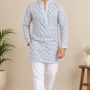 Puede incluir: Una kurta de manga larga en color azul claro con un patrón geométrico repetitivo en blanco y beige, cuello mao y una tapeta blanca con bordado vertical, combinada con pantalones blancos lisos y zapatos sin cordones marrones.
