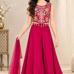 Puede incluir: Un top corto sin mangas de color magenta con intrincados bordados florales multicolores y un dobladillo con flecos de cuentas, combinado con pantalones anchos a juego y una dupatta magenta transparente.