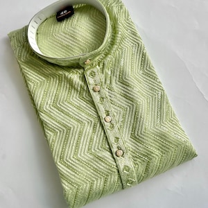 May include: A light green kurta featuring a chevron pattern with subtle sequin embellishments. The garment has a mandarin collar, a buttoned placket with five gold-toned buttons, and a size 40 label visible inside the neckline.