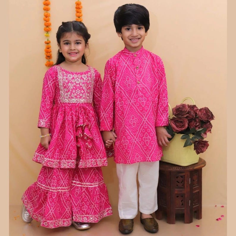 May include: A bright pink two-piece outfit featuring a long-sleeved tunic with silver embroidery and matching flared pants, alongside a long-sleeved pink patterned kurta paired with plain white trousers, both showcasing traditional bandhani-style prints.