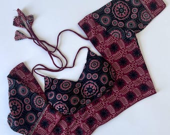 May include: A two-piece set consisting of a halter-style bikini top and matching leggings. Both pieces feature a dark black and deep maroon fabric with a repeating circular mandala-inspired pattern. The top has thin tie straps with tassels.