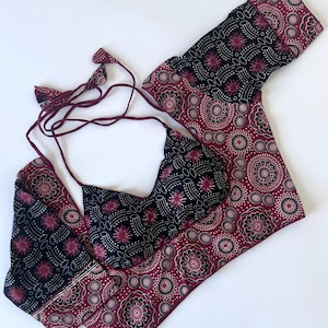 May include: A two-piece set with a black, burgundy, and cream pattern. The set includes a halter top with tie straps and a matching wrap. The fabric displays a repeating floral and geometric pattern.