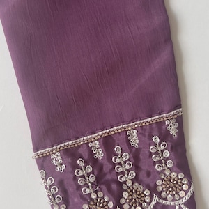 Puede incluir: Una manga larga de color morado intenso con tela texturizada. El pu&ntilde;o est&aacute; adornado con intrincados bordados plateados, cuentas met&aacute;licas y patrones de lentejuelas circulares dispuestos en un dise&ntilde;o festoneado en el borde inferior.
