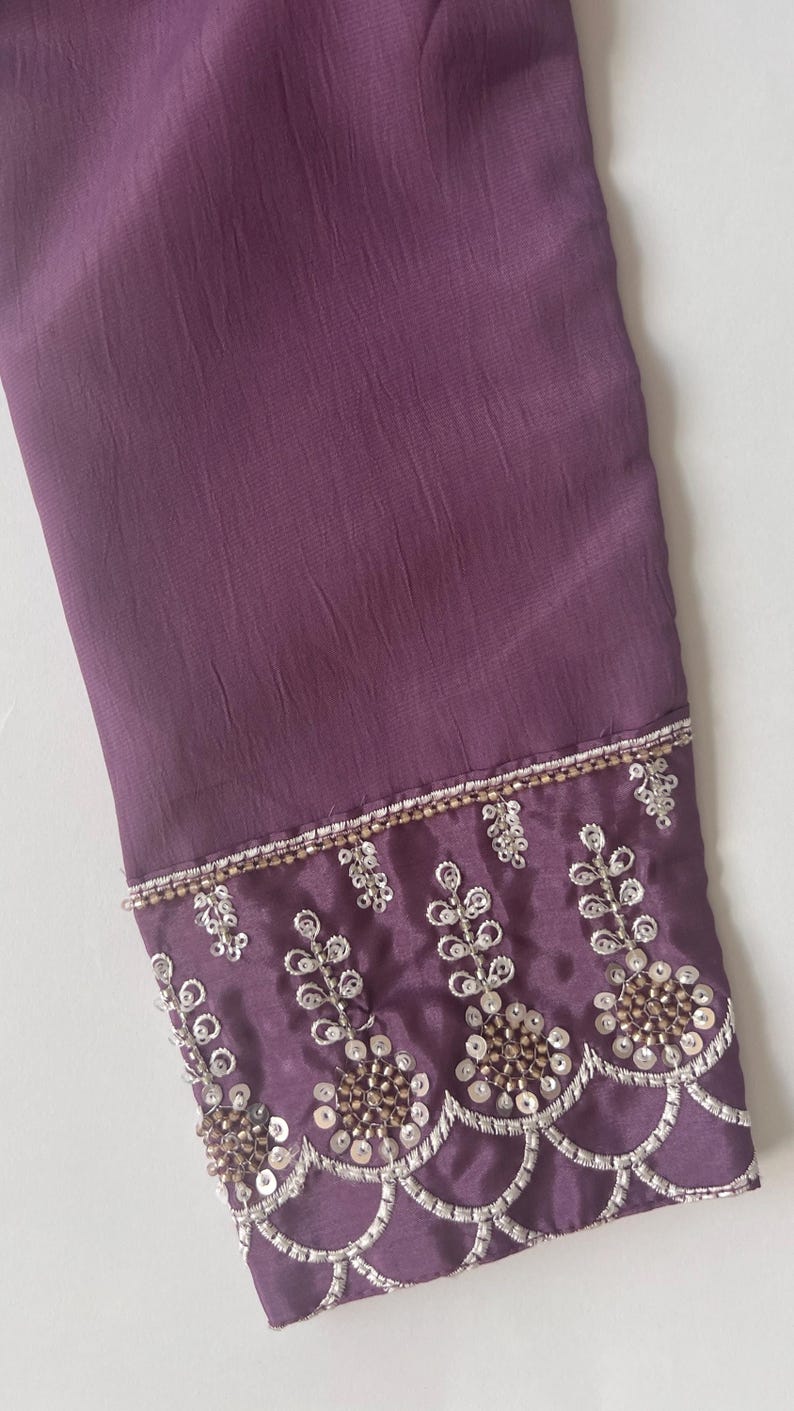 Puede incluir: Una manga larga de color morado intenso con tela texturizada. El pu&ntilde;o est&aacute; adornado con intrincados bordados plateados, cuentas met&aacute;licas y patrones de lentejuelas circulares dispuestos en un dise&ntilde;o festoneado en el borde inferior.