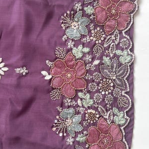 Puede incluir: Una tela de color morado intenso con un borde bordado intrincado con motivos florales en tonos rosa viejo, verde salvia y plata met&aacute;lica. El dise&ntilde;o incluye hilos detallados, peque&ntilde;as lentejuelas transparentes y cuentas en el borde festoneado.