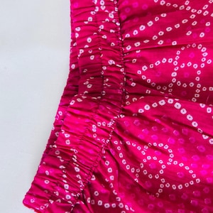 May include: A vibrant fuchsia garment featuring an elasticized waistband and a repeating white tie-dye pattern of small, circular dots arranged in flowing, interconnected wave-like lines across the fabric surface.