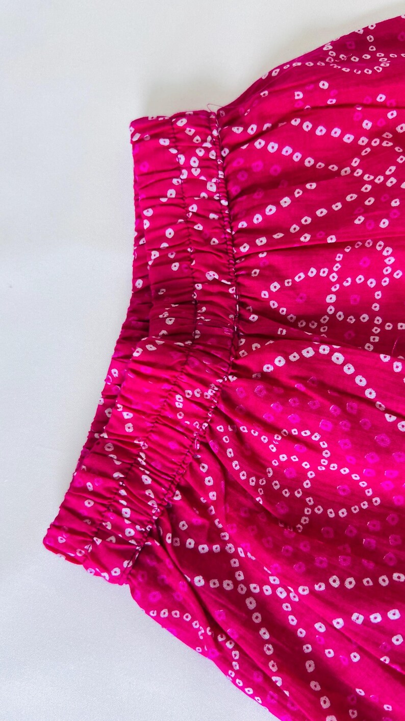 May include: A vibrant fuchsia garment featuring an elasticized waistband and a repeating white tie-dye pattern of small, circular dots arranged in flowing, interconnected wave-like lines across the fabric surface.