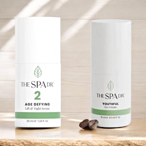 May include: Two white cylindrical skincare product bottles with green accents. One reads "THE SPA DR 2 AGE DEFYING Lift & Tight Serum 30 ml e 1 US fl. Oz." The other says "THE SPA DR YOUTHFUL Eye Cream 15 ml e 0.5 US fl. Oz."