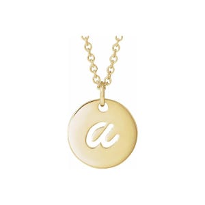 Könnte beinhalten: Eine goldfarbene Halskette mit einem kreisförmigen Anhänger mit einem ausgeschnittenen Buchstaben "a". Der Anhänger hängt an einer filigranen Kette. Die Halskette wird vor weißem Hintergrund präsentiert.
