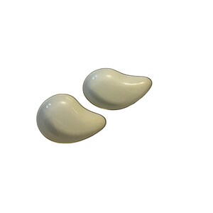 May include: A pair of off-white, teardrop-shaped earrings with a gold-colored trim. The earrings have a smooth, glossy finish and are set against a white background. These earrings are a simple yet elegant accessory.