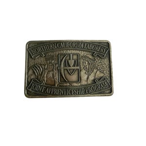 May include: A rectangular, silver-coloured belt buckle with the words "NORTHERN CALIFORNIA LABORERS" and "JOINT APPRENTICESHIP PROGRAM" engraved on it. The buckle features two figures and a central emblem.