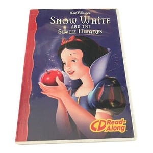 Puede incluir: Una funda de DVD de "Blancanieves y los Siete Enanitos" de Walt Disney. La portada presenta una ilustración de Blancanieves sosteniendo una manzana roja. El texto "CD Read Along" es visible en la esquina inferior derecha.