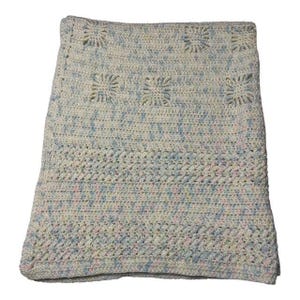 Puede incluir: Una manta hecha a mano, tejida a ganchillo, en una suave paleta de colores pastel de blanco, azul y rosa. La manta presenta un diseño texturizado con patrones cuadrados y un borde decorativo. La estética general es acogedora e invitante.
