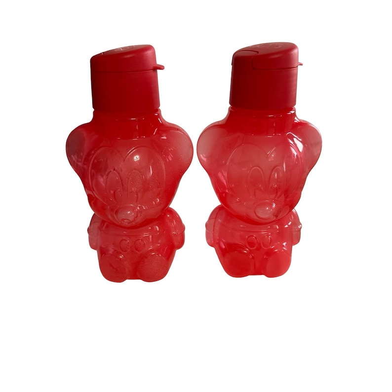 May include: Two translucent red plastic water bottles shaped like a cartoon bear character. Each bottle features a molded face, a rounded body, and a solid red flip-top cap. The design includes embossed details on the front of the bear-shaped container.