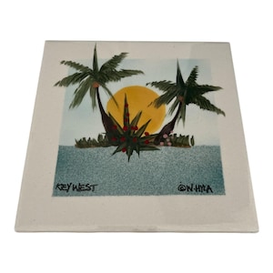 Könnte beinhalten: Quadratische Keramikfliese mit einer tropischen Szene mit Palmen, einer gelben Sonne und blauem Wasser. Die Worte "KEY WEST" und "@N.HYA" sind auf die Fliese gedruckt. Das Kunstwerk ist in Grün-, Gelb-, Blau- und Brauntönen gehalten.