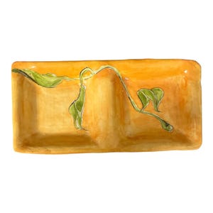 Puede incluir: Plato de cerámica rectangular con dos compartimentos. El plato está pintado en tonos amarillos y naranjas, con un diseño de vid y hojas verdes. Ideal para servir aperitivos o entremeses.